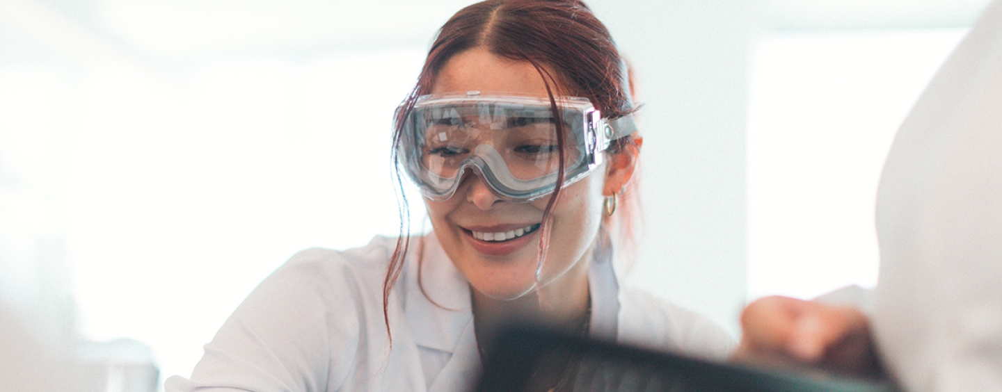 Person wearing goggles is smiling in a scientific lab.