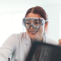 Person wearing goggles is smiling in a scientific lab.